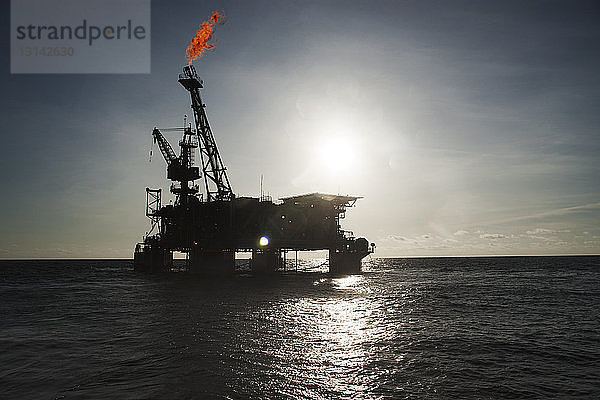 Silhouette einer Ölplattform im Meer mit Brand