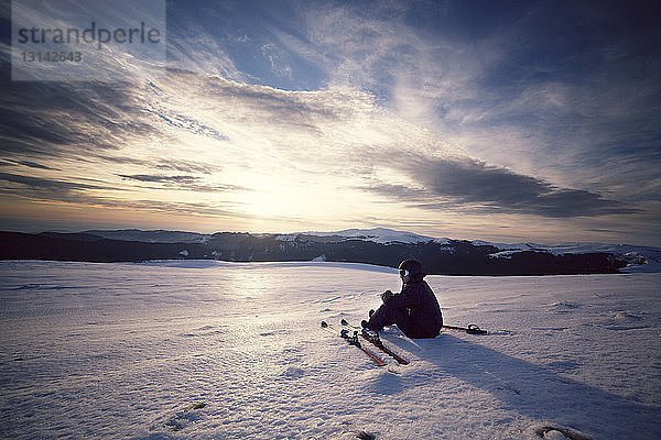 Skifahrer  der auf schneebedecktem Berg sitzend gegen den Himmel blickt