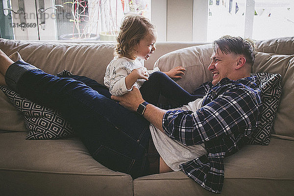 Vater spielt zu Hause mit Mädchen auf dem Sofa