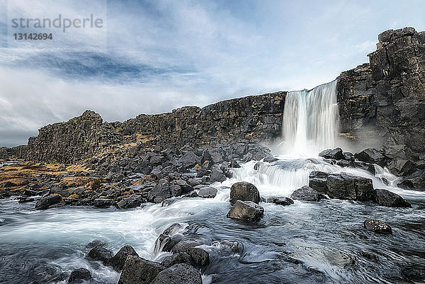 Szenische Ansicht eines Wasserfalls durch eine Felsklippe vor bewölktem Himmel