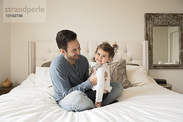 Porträt einer fröhlichen Tochter mit dem Vater zu Hause auf dem Bett sitzend
