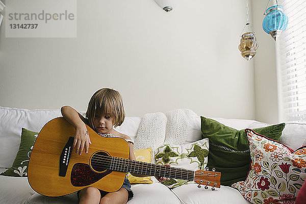 Mädchen spielt Gitarre  während sie zu Hause auf dem Sofa sitzt