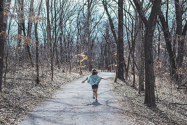 Unbekümmertes Mädchen mit ausgestreckten Armen auf Feldweg mitten im Wald rennend