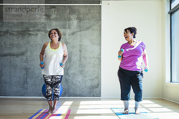 Glückliche Freundinnen in voller Länge mit Hanteln beim Üben an der Wand im Yogastudio