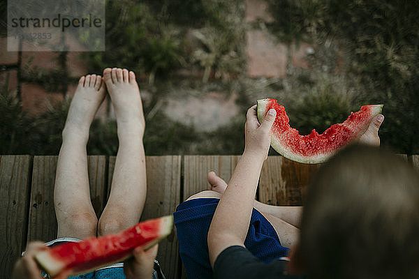 Draufsicht auf Brüder  die Wassermelone essen  während sie auf der Veranda sitzen