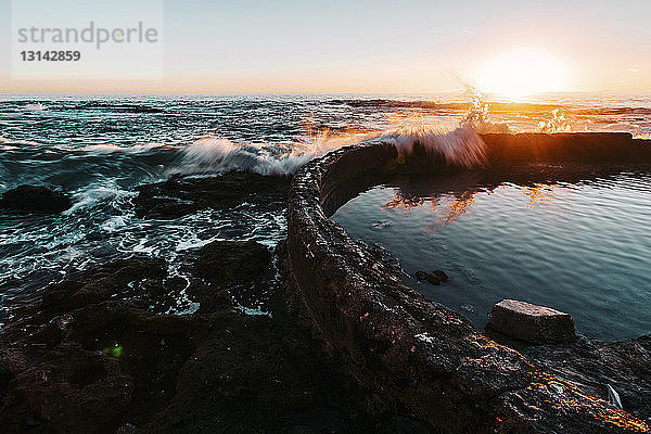 Wellen  die bei Sonnenuntergang auf die Stützmauer im Meer spritzen