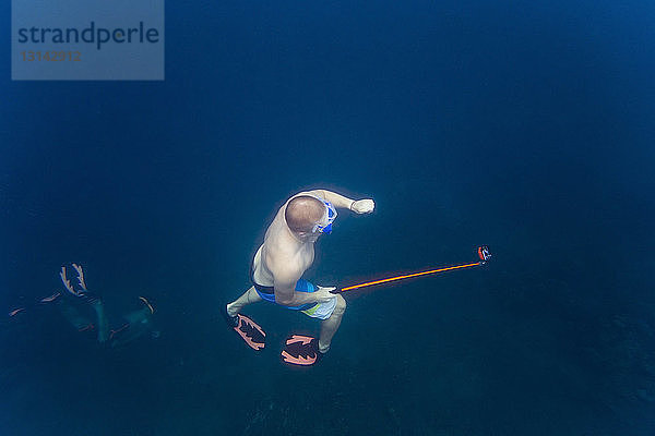 Hochwinkelaufnahme eines Mannes  der ein Einbeinstativ hält  während er mit Freunden unter Wasser schwimmt