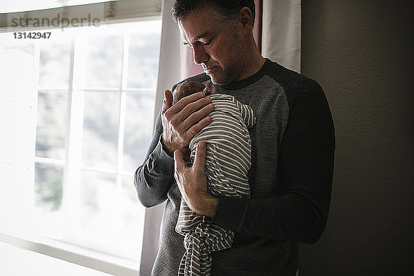 Vater trägt neugeborene Tochter  während er zu Hause steht