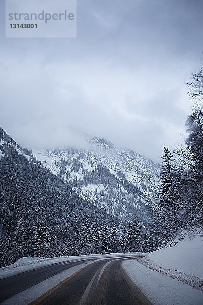 Landstraße führt zum schneebedeckten Berg gegen bewölkten Himmel