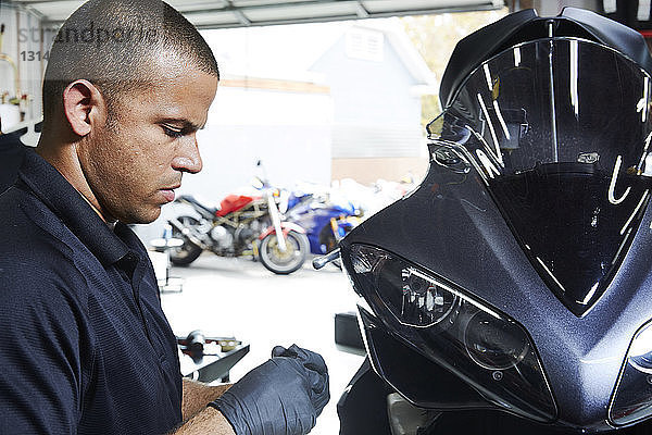 Zuversichtlicher Arbeiter bei der Arbeit auf dem Motorrad in der Werkstatt