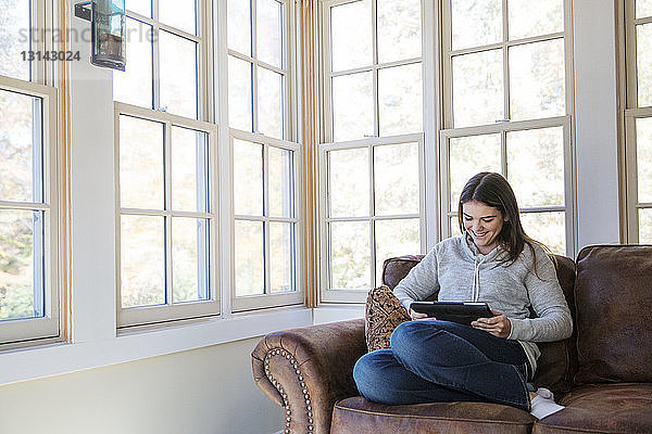 Lächelnde Frau benutzt Tablet-Computer  während sie zu Hause auf dem Sofa sitzt