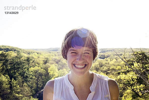 Porträt einer fröhlichen Frau an einem sonnigen Tag vor Bäumen