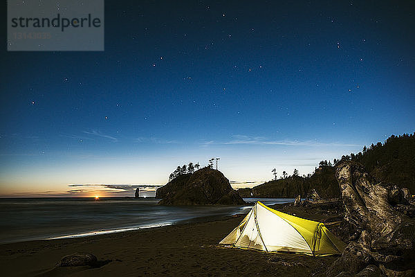 Beleuchtetes Zelt am Meeresufer vor blauem Himmel in der Abenddämmerung