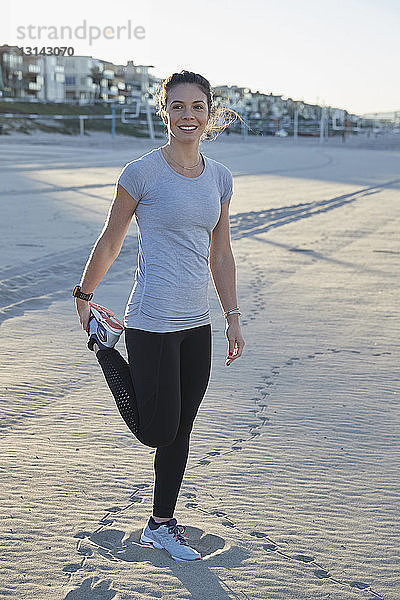 Lächelnde Frau in voller Länge mit ausgestrecktem Bein am Strand