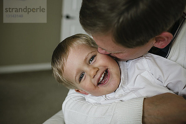 Glücklicher Vater küsst Sohn  während er zu Hause sitzt