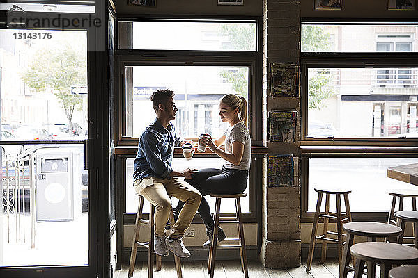 Lächelndes Paar trinkt Kaffee und unterhält sich an den Glasfenstern eines Cafés