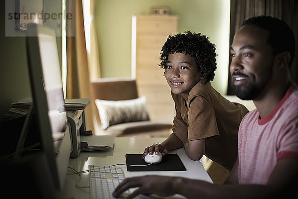 Vater und Sohn benutzen Computer  während sie zu Hause sitzen