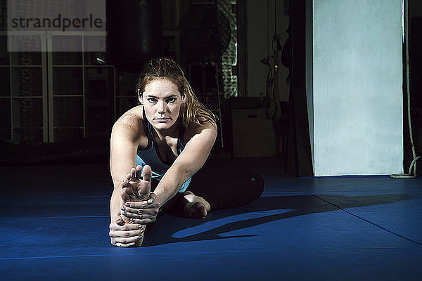 Porträt einer Sportlerin  die sich beim Training im Fitnessstudio dehnt