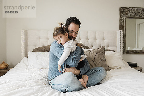Porträt einer traurigen Tochter  die vom Vater zu Hause auf dem Bett umarmt wird