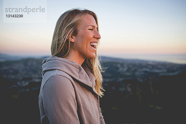 Seitenansicht einer glücklichen Frau  die bei Sonnenuntergang auf einem Berg gegen den Himmel steht