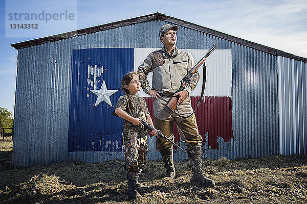 Familie hält Gewehr  während sie auf dem Feld gegen die texanische Flagge steht