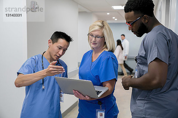 Arzt diskutiert mit Kollegen über Laptop-Computer  während er im Krankenhauskorridor steht