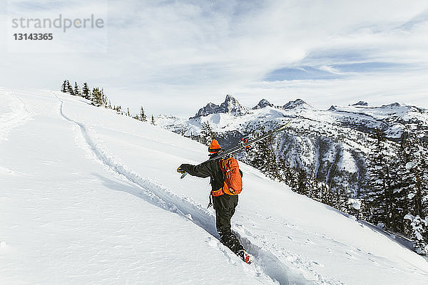 Wanderer trägt Ski auf der Schulter  während er einen schneebedeckten Berg besteigt