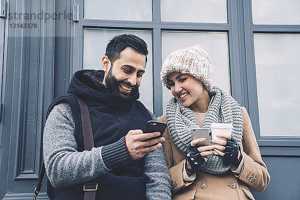 Mann zeigt seiner Freundin ein Handy  während er sich an ein Gebäude in der Stadt lehnt