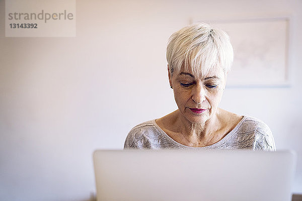 Ältere Frau benutzt Laptop-Computer zu Hause an der Wand