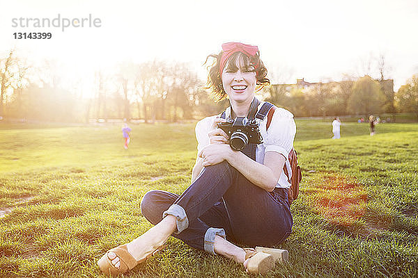 Porträt einer glücklichen Frau mit Kamera im Park sitzend