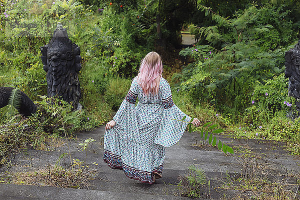 Rückansicht einer Frau in einem Kleid  die sich auf Stufen im Wald nach unten bewegt