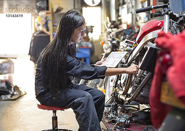 Seitenansicht einer Frau  die während einer Fahrradreparatur in der Werkstatt ein digitales Tablett hält