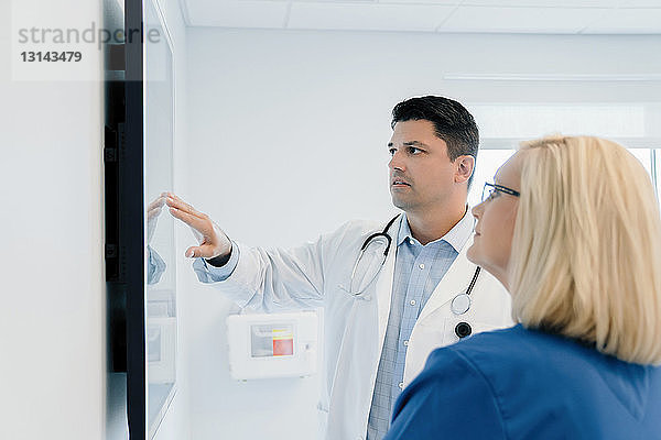 Arzt zeigt auf Flachbildschirm  während er mit einer Kollegin im Krankenhaus diskutiert