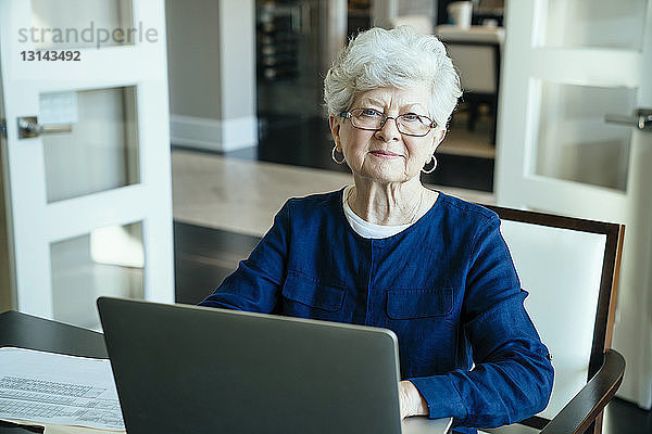 Porträt einer älteren Frau  die zu Hause einen Laptop benutzt