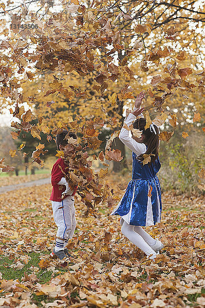 Glückliche Geschwister spielen mit Herbstlaub im Park