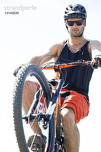 Mann führt Stunt mit Fahrrad gegen klaren Himmel an einem sonnigen Tag aus