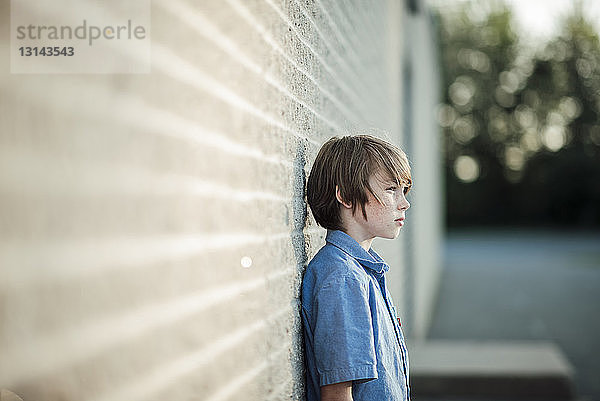 Nachdenklicher Junge schaut weg  während er sich an die Wand lehnt