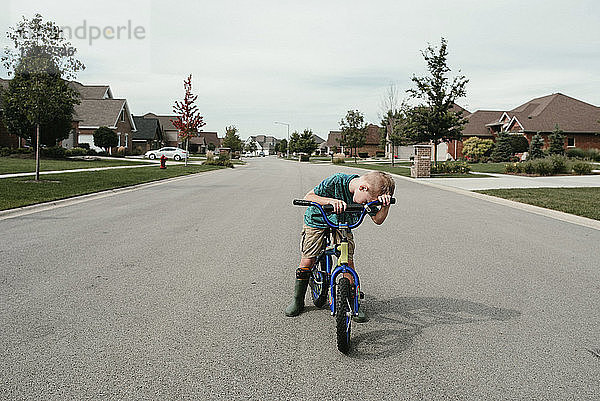 Junge fährt Fahrrad auf Straße gegen bewölkten Himmel