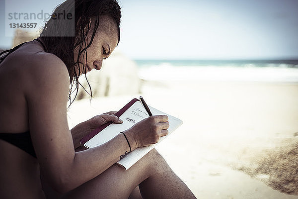 Seitenansicht einer Frau  die am Strand sitzend gegen den Himmel zeichnet