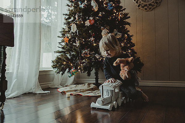 Mädchen spielt zu Hause mit Spielzeug gegen den Weihnachtsbaum