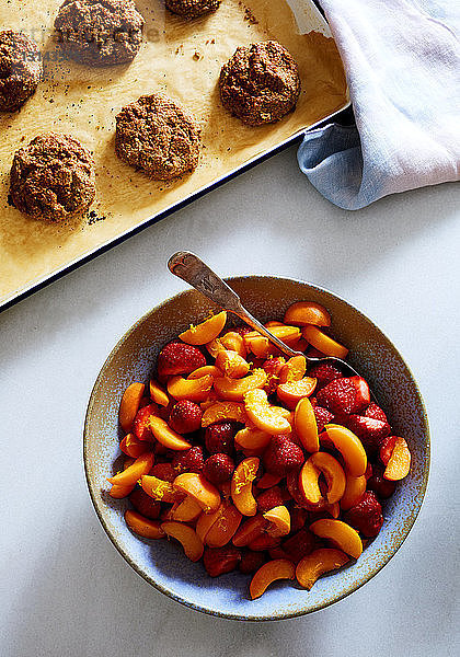 Draufsicht auf Pfirsichscheiben und Erdbeeren in einem Behälter mit Keksen auf weißem Hintergrund