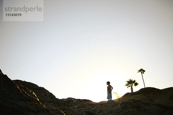 Tiefwinkelaufnahme eines Jungen  der auf Felsformationen vor klarem Himmel am Laguna Beach steht