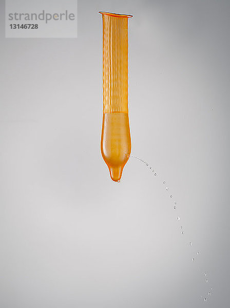 Orangefarbenes Kondom mit auslaufender Flüssigkeit