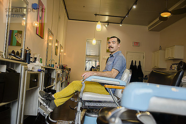 Junger Mann sitzt auf einem Stuhl im Friseursalon