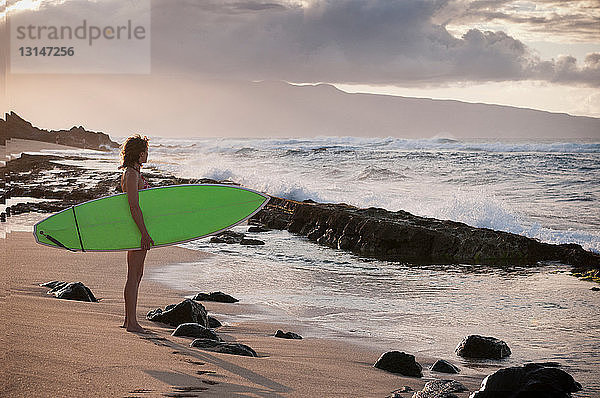Surfer trägt Surfbrett am Strand