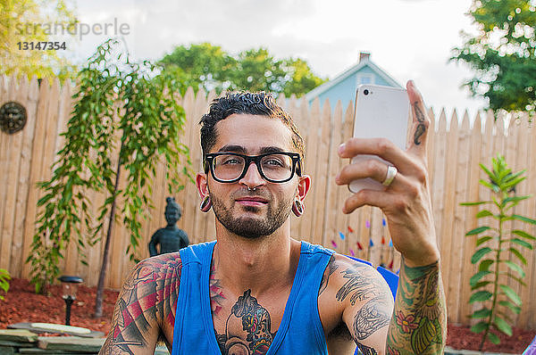 Mittelgroßer erwachsener Mann  der im Garten ein Selfie mit seinem Smartphone macht