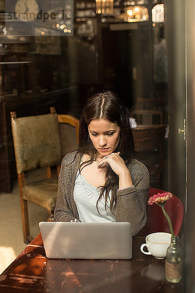 Mittlere erwachsene Frau sitzt am Tisch und benutzt einen Laptop  Hand am Kinn