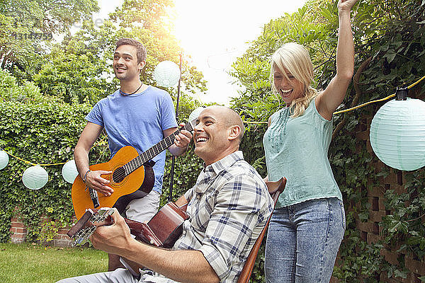 Männliche Freunde spielen akustische Gitarre im Garten und junge Frau tanzt