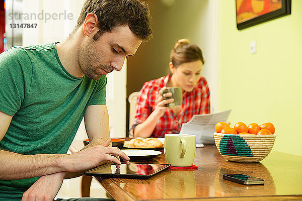 Junges Paar beim Frühstück  Mann mit digitalem Tablet