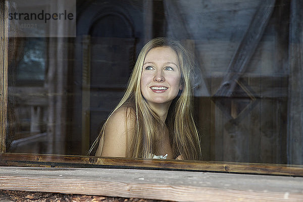 Junge Frau mit nackten Schultern schaut aus dem Fenster der Sauna